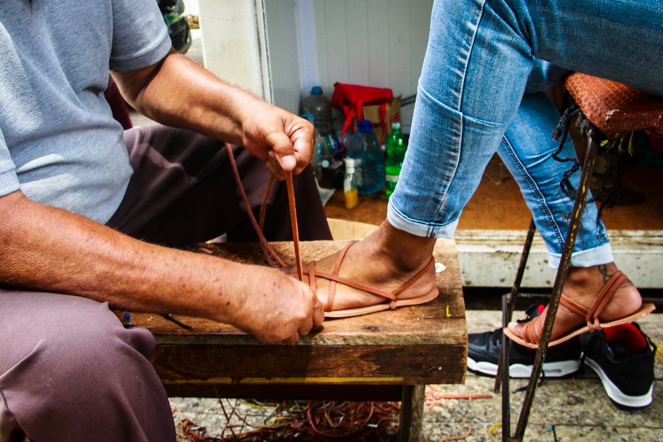 A craftsman skillfully ties leather straps on handmade sandals.